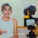 Elderly woman vlogging indoors, engaging with her audience through a camera.